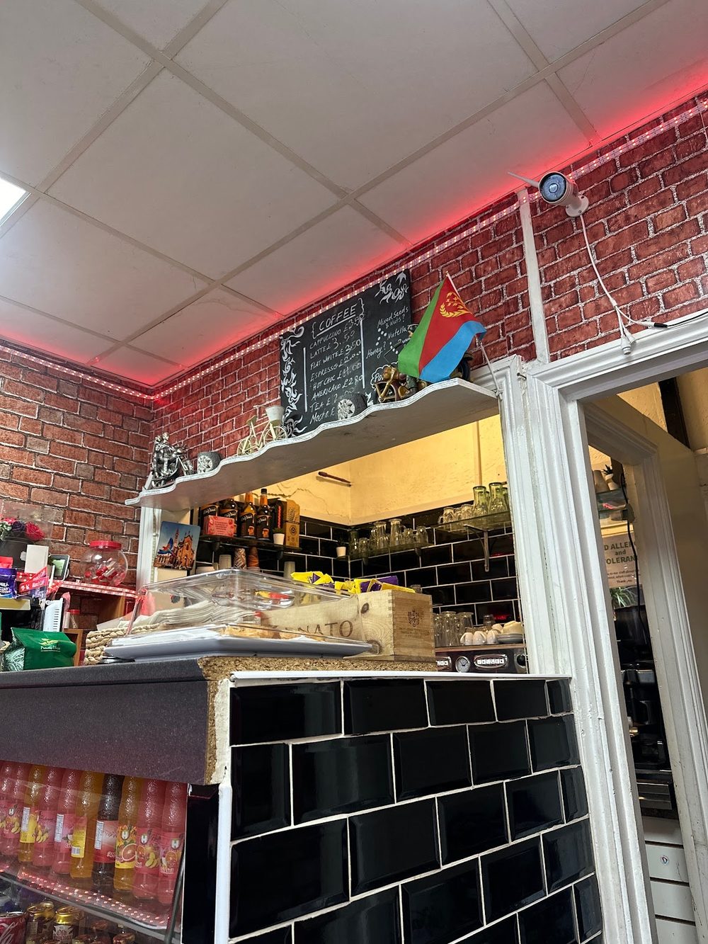 The counter at Manu's Cafe, exposed brick with pink neon strip lighting and a black-tiled serving hatch